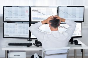 Trader With Hands On Head Looking At Graphs On Screens