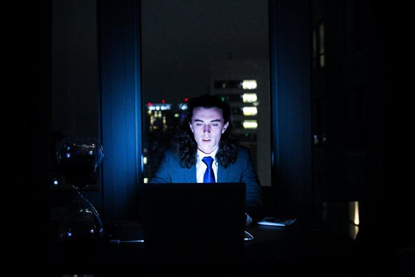 Man in suit sitting a trading laptop in a dark office